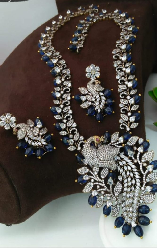 Raw catalogue photo of a sapphire-and-diamond peacock necklace set on a display cushion